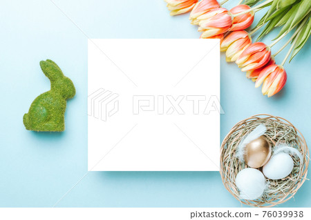 Easter flower. Golden, white colour egg in basket with spring tulips, feathers on pastel blue background in Happy Easter decoration. Festive design with copy space. 76039938