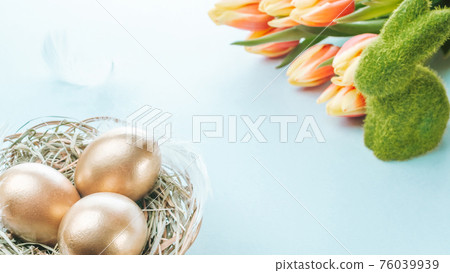 Easter eggs gold. Golden colour egg in basket with spring tulips, white feathers on pastel blue background in Happy Easter decoration. Congratulatory easter design. 76039939