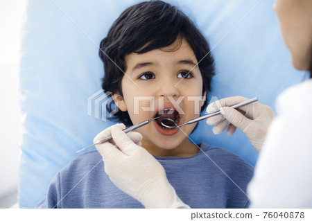 Cute arab boy sitting at dental chair with open mouth during oral checking up with doctor. Visiting dentist office. Stomatology concept 76040878