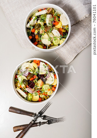 Vegetarian salad with vegetables, mozzarella and fresh herbs in round white bowls on a light background. Organic delicious and healthy food. Vertical shot. Top view 76041101