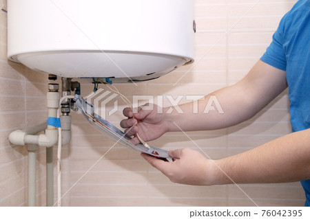 The boiler repair technician uses an adjustable wrench to unscrew or tighten the nut on the pipe. Installing a water heater or dismantling a damaged boiler for later repair. 76042395