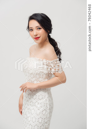 Beautiful Asian young woman in white dress posing on the white background. Beauty, fashion. Haircare. Cosmetics. Beautiful Asian young woman in white dress posing on the white background. Beauty, fashion. Haircare. Cosmetics. 76042468