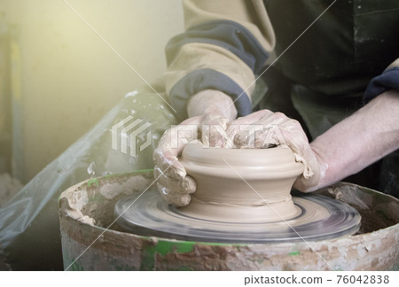 Hands of a potter on a pottery wheel close-up. Old traditional art, handmade, clay and ceramic production. Pottery workshop in subdued soft light Hands of a potter on a pottery wheel close-up. Old traditional art, handmade, clay and ceramic production. Pottery workshop in subdued soft light 76042838