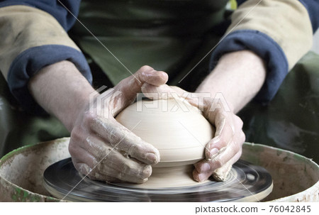 Hands of a potter on a pottery wheel close-up. Old traditional art, handmade, clay and ceramic production. Pottery workshop in subdued soft light Hands of a potter on a pottery wheel close-up. Old traditional art, handmade, clay and ceramic production. Pottery workshop in subdued soft light 76042845