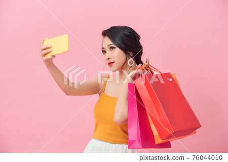 Portrait smiling woman holding packages bags with purchases after shopping doing selfie shot on mobile phone Portrait smiling woman holding packages bags with purchases after shopping doing selfie shot on mobile phone 76044010
