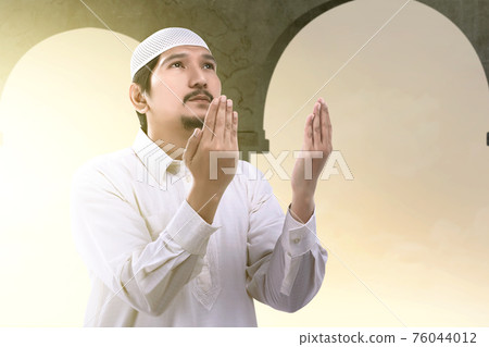 Asian Muslim man standing while raised hands and praying 76044012