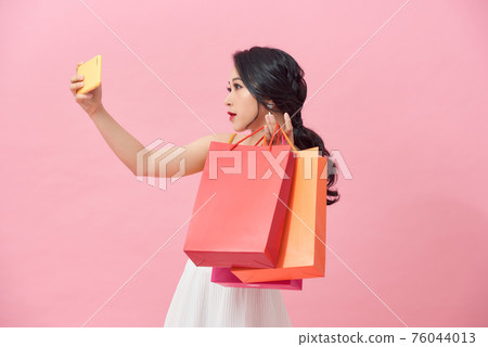 Happy pretty young woman with shopping bags makes photo self-portrait on the smartphone over colorful wall 76044013