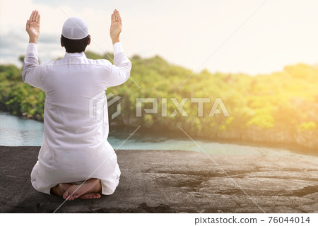 Rear view of Asian Muslim man sitting while raised hands and praying Rear view of Asian Muslim man sitting while raised hands and praying 76044014