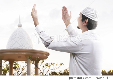 Asian Muslim man standing while raised hands and praying Asian Muslim man standing while raised hands and praying 76044018
