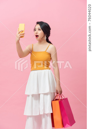 Surprised young woman with mobile phone and shopping bags on color background Surprised young woman with mobile phone and shopping bags on color background 76044020