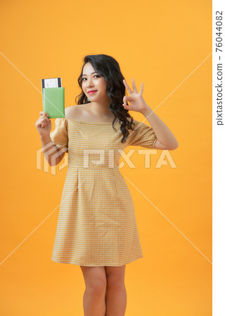 Beautiful portrait young asian woman smiling gesture ok over yellow background, holding passport. Beautiful portrait young asian woman smiling gesture ok over yellow background, holding passport. 76044082