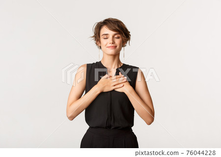 Image of nostalgic happy young woman close eyes and holding hands on heart while remember something, smiling pleased, white background 76044228