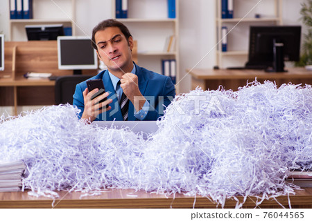 Young male employee and a lot of cut papers in the office 76044565