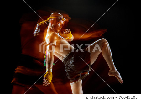 Young man thai boxer training over dark background in neon mixed light. Young man thai boxer training over dark background in neon mixed light. 76045103