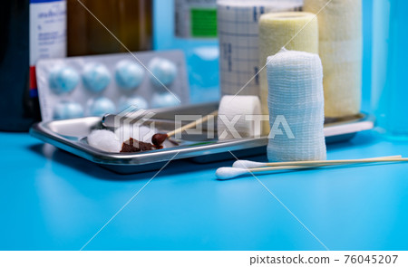 Wound care dressing set. Selective focus cotton stick and elastic conforming bandage, stainless steel plate on blur forceps, bandage, cotton ball with alcohol. Medical supply on blue background. 76045207