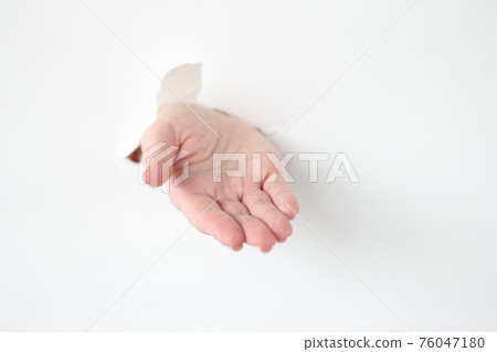 Woman hand reaches out through the hole in white paper 76047180
