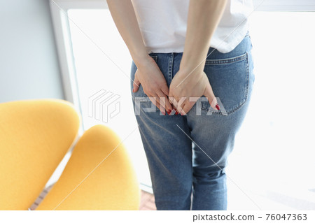 Woman stands and embarrassedly holds her hands on her buttocks 76047363