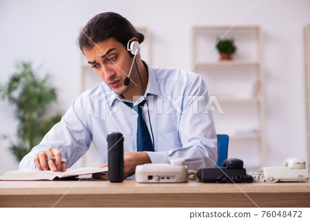 Young male call center operator working at his desk Young male call center operator working at his desk 76048472