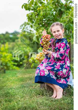 Little girl with grapes in the garden. 76048809