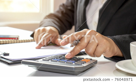 Close-up of businessmen or accountants holding a pen and pressing on the calculator to calculate business information, accounting documents, business ideas. Close-up of businessmen or accountants holding a pen and pressing on the calculator to calculate business information, accounting documents, business ideas. 76048971
