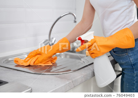 Woman cleaning sink with rag and detergent in kitchen. Woman cleaning sink with rag and detergent in kitchen. 76049403