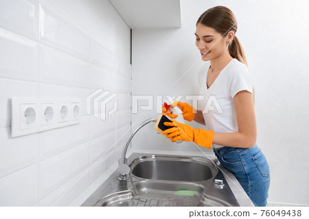Smiling woman cleaning faucet kitchen sink. Smiling woman cleaning faucet kitchen sink. 76049438