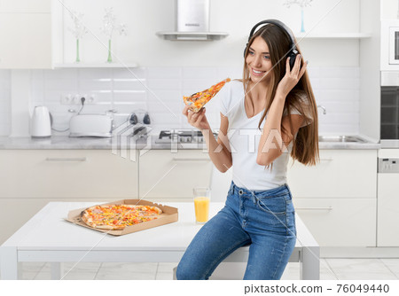 Woman sitting in headphone and eating tasty pizza. Woman sitting in headphone and eating tasty pizza. 76049440