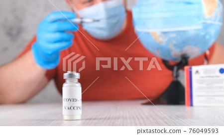 vial with a vaccine against the coronavirus, in the background a man is vaccinating the planet, the vial with a vaccine against the coronavirus, in the background a man is vaccinating the planet, the 76049593