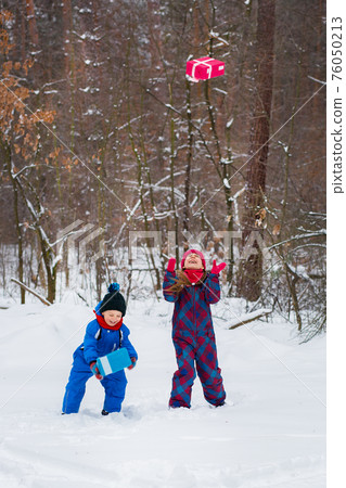 Happy children in a winter snow-covered forest with gift boxes. Happy children in a winter snow-covered forest with gift boxes. 76050213