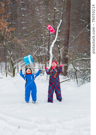 Happy children in a winter snow-covered forest with gift boxes. 76050214