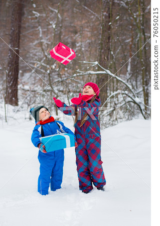 Happy children in a winter snow-covered forest with gift boxes. 76050215