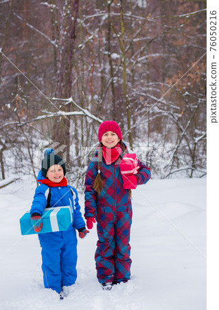 Happy children in a winter snow-covered forest with gift boxes. Happy children in a winter snow-covered forest with gift boxes. 76050216