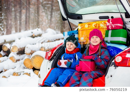 Joyful children enjoy many Christmas presents in car trunk. 76050219