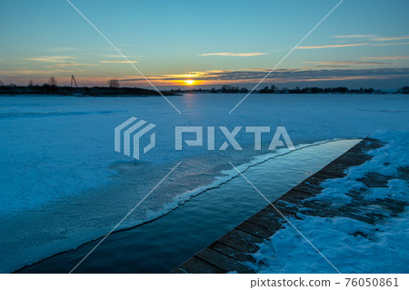 Wooden pier and a frozen lake during the sunset 76050861