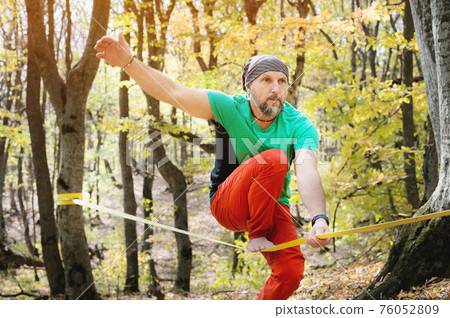 Autumn forest. middle aged athletic man practices slackline balance in autumn forest. Autumn forest. middle aged athletic man practices slackline balance in autumn forest. 76052809