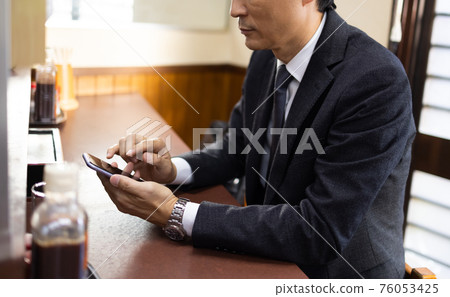 Office worker looking at a smartphone at a set meal shop 76053425