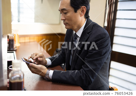 Office worker looking at a smartphone at a set meal shop 76053426