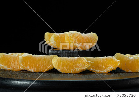 Slices of peeled orange on a black background. 76053726