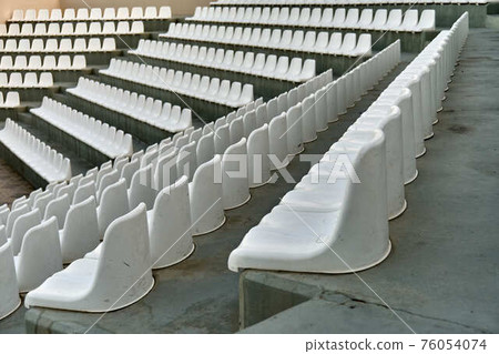 Chairs made of white plastic on spectator places of stadium 76054074