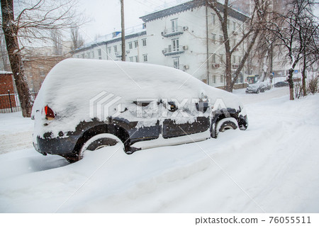 Vehicles covered with snow in a winter blizzard in the parking lot. Vehicles covered with snow in a winter blizzard in the parking lot. 76055511