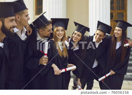 Smiling students in black gowns and square caps with diplomas having fun after graduation ceremony Smiling students in black gowns and square caps with diplomas having fun after graduation ceremony 76056156