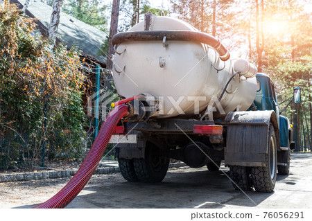 Close-up pipe hose of sewage truck car engine emptying home sewerage tank. Septic cleaning vacuum service and maintenance suburban countryside home. Suction vehicle cleaner machine pumping drainage 76056291