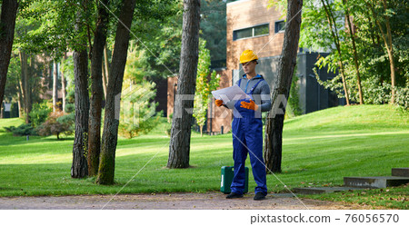 Full length of young builder standing outdoors with blueprint while working on cottage construction 76056570