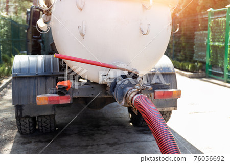 Close-up pipe hose of sewage truck car engine emptying home sewerage tank. Septic cleaning vacuum service and maintenance suburban countryside home. Suction vehicle cleaner machine pumping drainage Close-up pipe hose of sewage truck car engine emptying home sewerage tank. Septic cleaning vacuum service and maintenance suburban countryside home. Suction vehicle cleaner machine pumping drainage 76056692