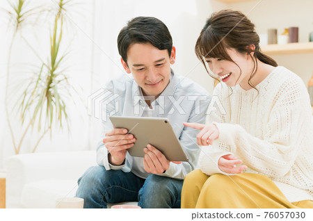 A young couple sitting on the sofa in the living room and looking at the tablet A young couple sitting on the sofa in the living room and looking at the tablet 76057030