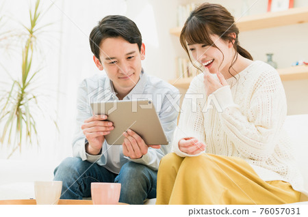 A young couple sitting on the sofa in the living room and looking at the tablet 76057031