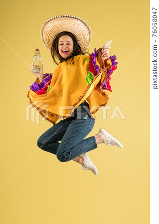 Young pretty girl in bright garment and sombrero isolated over yellow background Young pretty girl in bright garment and sombrero isolated over yellow background 76058047