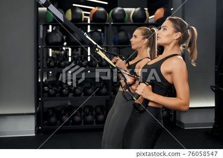 Cute women doing workout with trx system in gym. 76058547