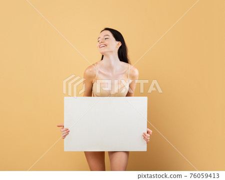 Smiling young female with vitiligo skin disorder holding white blank placard 76059413
