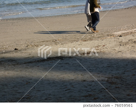 A couple walking on the beach and a shadow on the sand 76059561